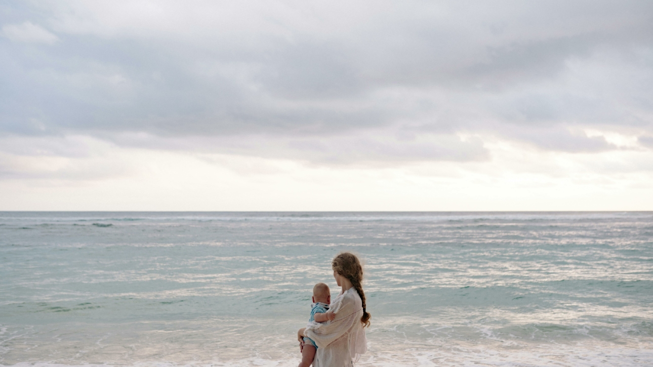 Femme avec son enfant dans les bras face à la mer