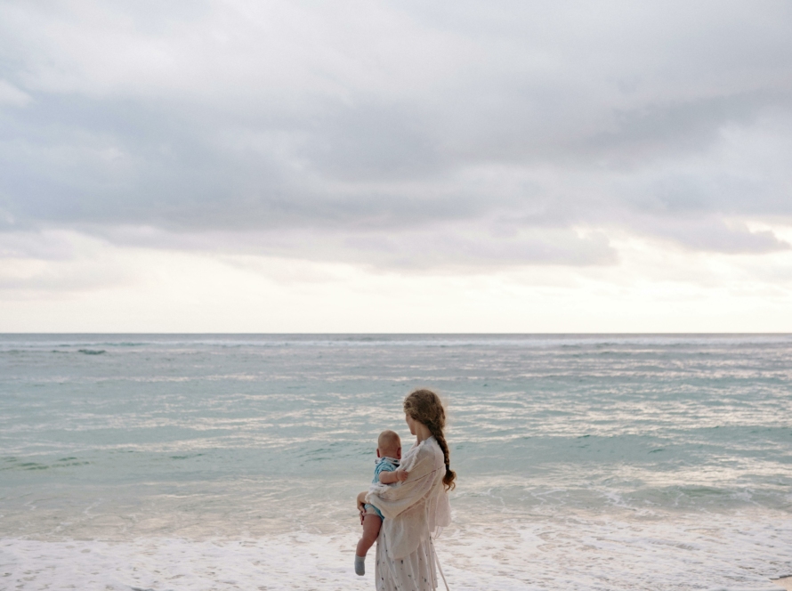 Femme avec son enfant dans les bras face à la mer