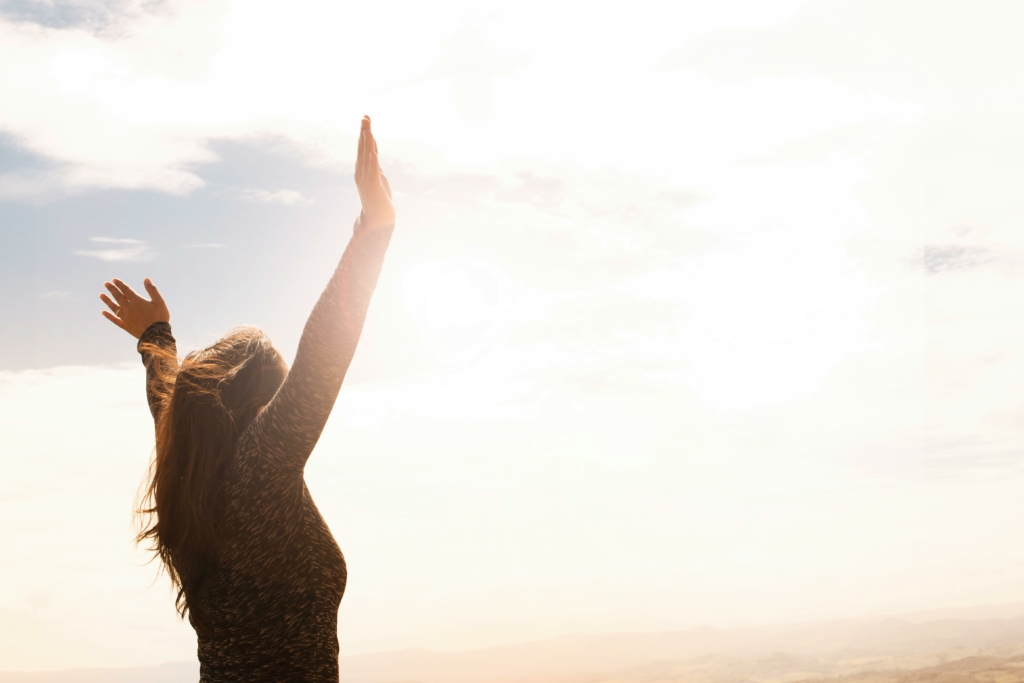 Femme les bras en l'aire devant le soleil, heureuse