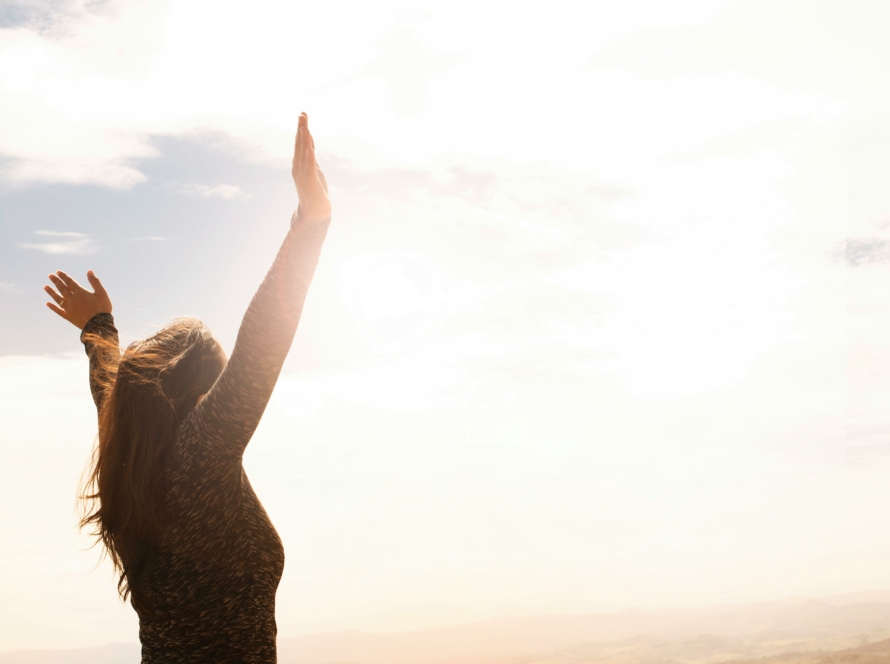 Femme les bras en l'aire devant le soleil, heureuse