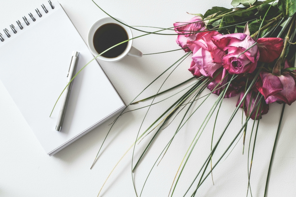 Photo avec un calepin, un stylo, une tasse de café et un bouquet de fleur allongé