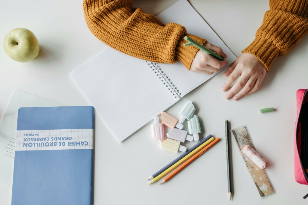 Stylos, cahier et enfant en train d'écrire