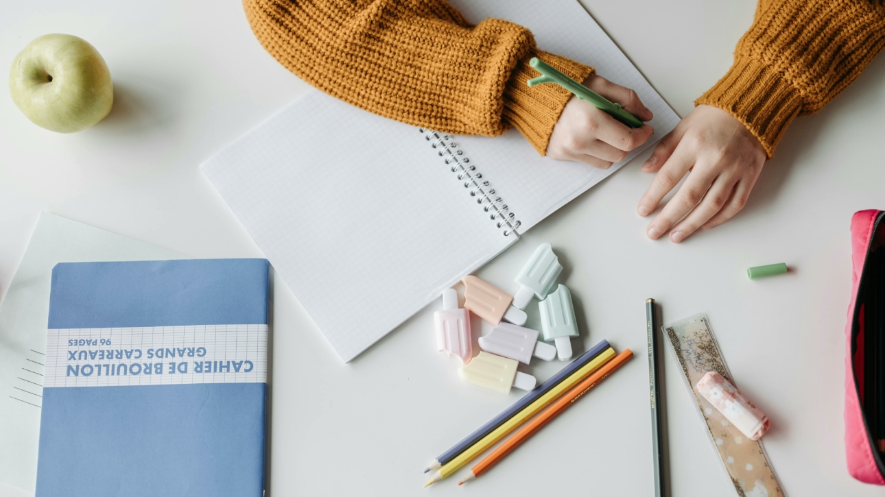 Stylos, cahier et enfant en train d'écrire