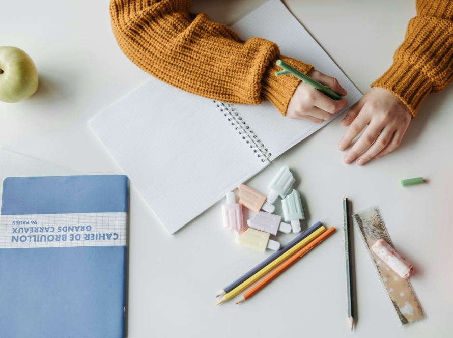 Stylos, cahier et enfant en train d'écrire